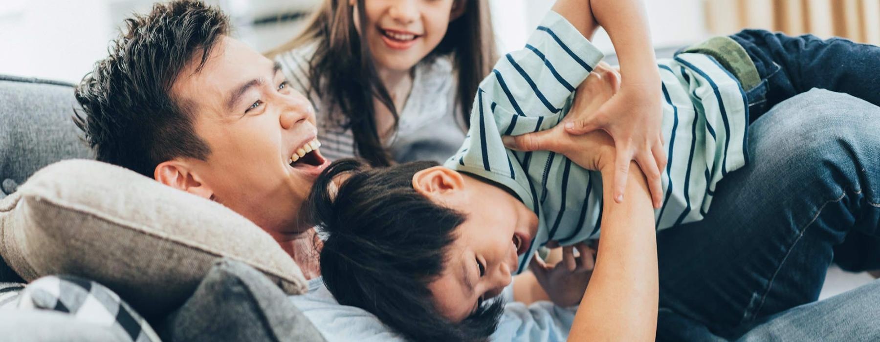 father plays on a couch with his young children